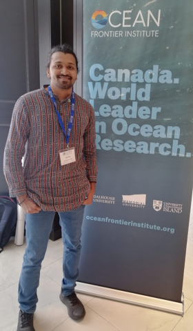 A student at a conference with a sign behind him that reads 